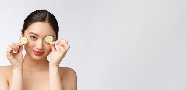 Натуральная домашняя свежая огуречная прокладка для глаз маски для лица Азиатская женщина, держащая огуречные прокладки и улыбка расслабиться с натуральной домашней