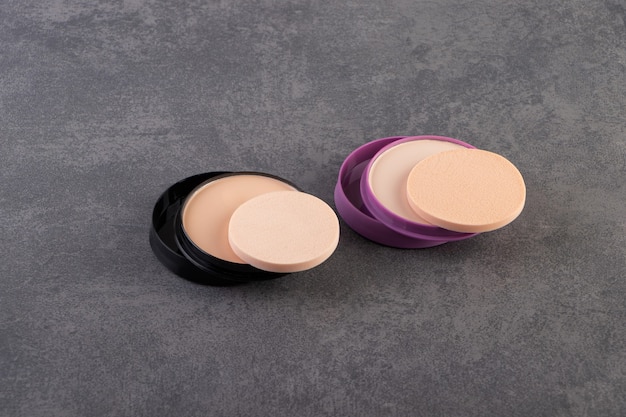 Natural powder foundation with sponges placed on stone surface.