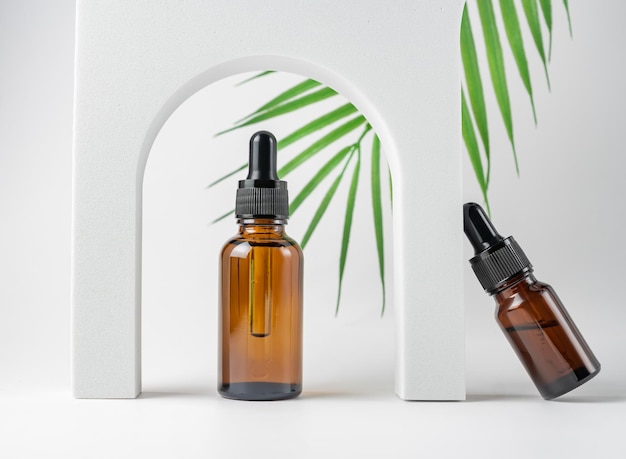 Natural skincare product in glass bottles with dropper. serum for woman facial skin. herbal mineral cosmetic, vitamin body oil on white stand. organic sometics presentation on tropical leaf background