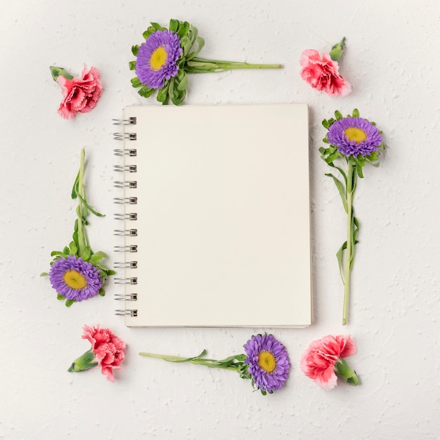 Free photo natural violet and carnation flowers frame with notepad