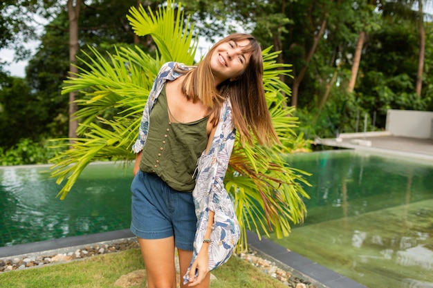 natural white woman posing  near  pool and palm trees.