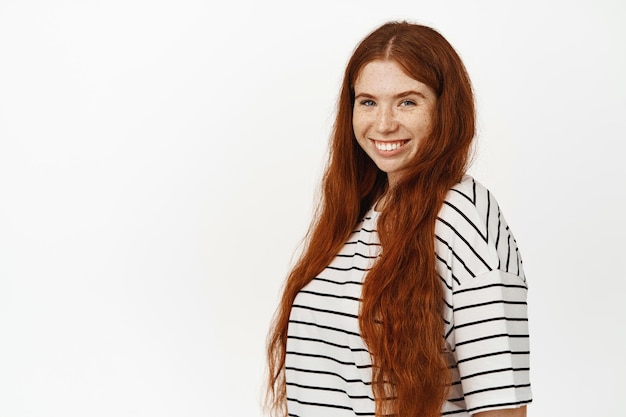 Bellezza naturale della donna. giovane bella ragazza dai capelli rossi con lunghi capelli rossi naturali, lentiggini e pelle pallida, sorridente con denti bianchi perfetti e sicura di sé, sfondo bianco