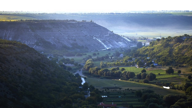 モルドバの自然、流れる川のある谷、それに沿った緑豊かな木々、野原と珍しい建物、岩だらけの丘