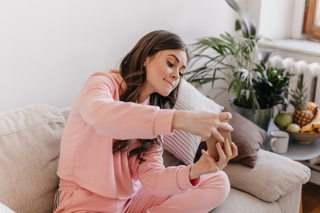 Naughty woman in tracksuit plays race on her phone, sitting on couch