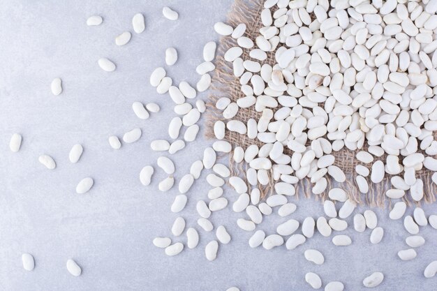 Navy beans scattered over a pieces of fabric on marble surface