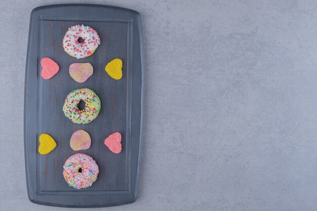 Navy wooden board with marmelades and donuts on marble surface