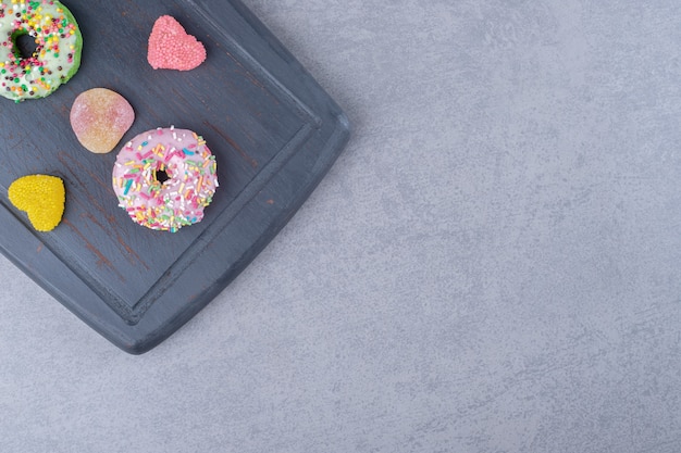 Navy wooden board with marmelades and donuts on marble surface