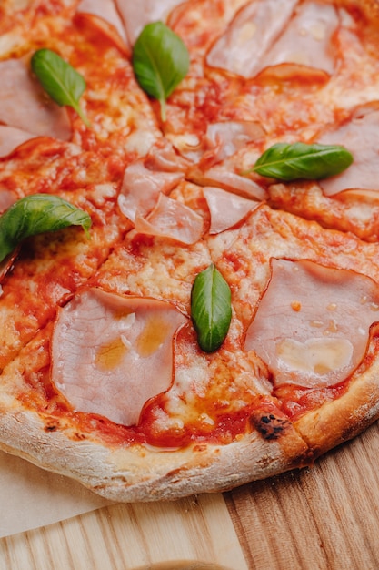 Neapolitan pizza with ham, cheese, arugula, basil, tomatoes sprinkled with cheese on a wooden board on a tablecloth in a cell with a place for text