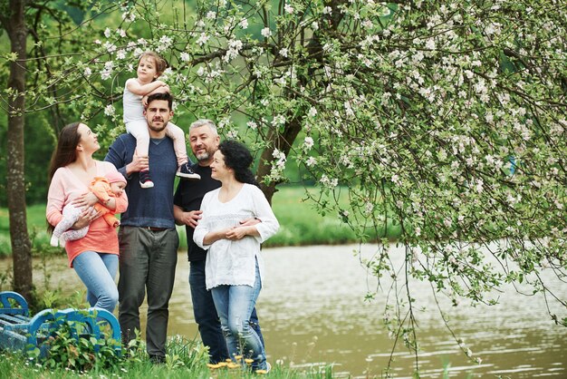 Near the bench and lake. Family photo. Full length portrait of cheerful people standing outdoors together