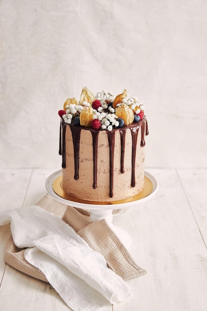 Аккуратный шоколадный торт с маленькими белыми цветами, ягодами и сухими листьями на нем