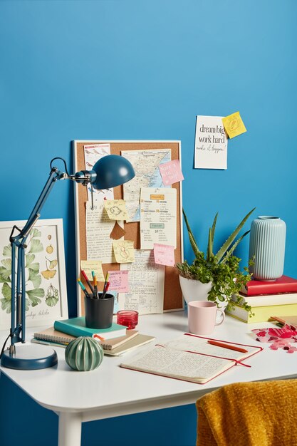 neat cozy workplace with notebook, desk lamp, coffee, indoor plant and sticky notes on white desk for education.