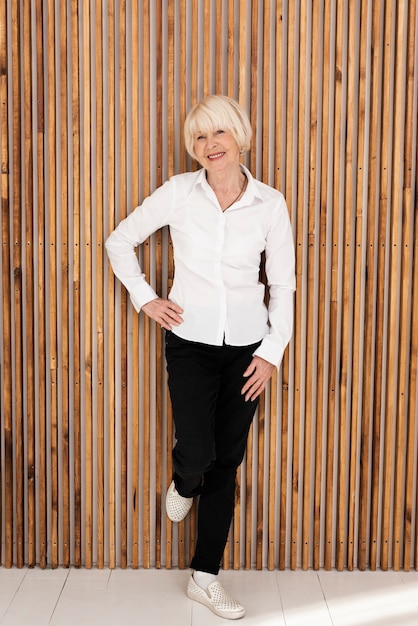 Neat old woman standing next to a wooden wall