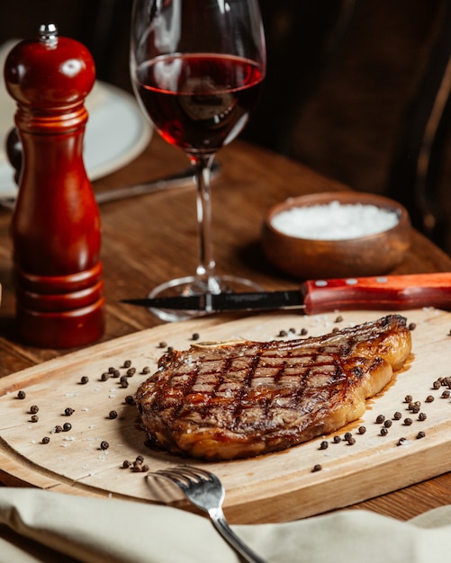 Foto gratuita bistecca ordinata su un supporto di legno con un bicchiere di vino rosso