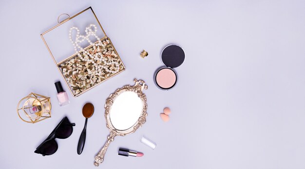 Necklace and flowers in the box; lipstick; blender; sunglasses; oval comb; compact powder; lipstick and hand mirror on purple background