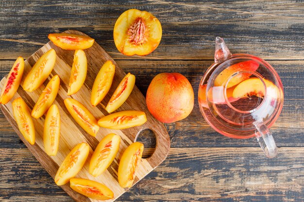 Nectarine slices with drink on wooden and cutting board table, top view.