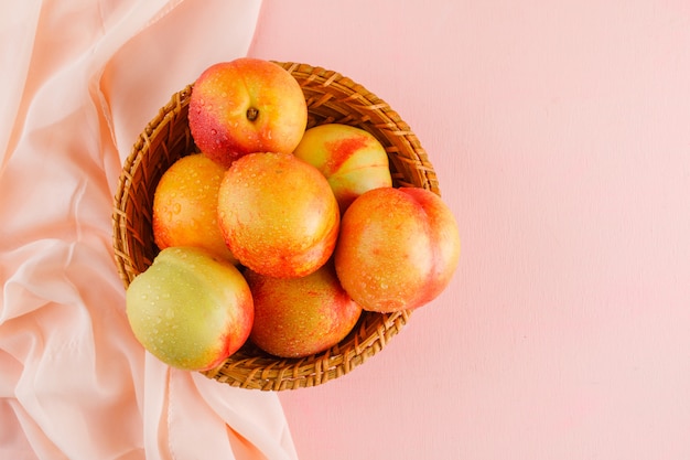 Nectarines in a basket on pink and textile surface, flat lay.