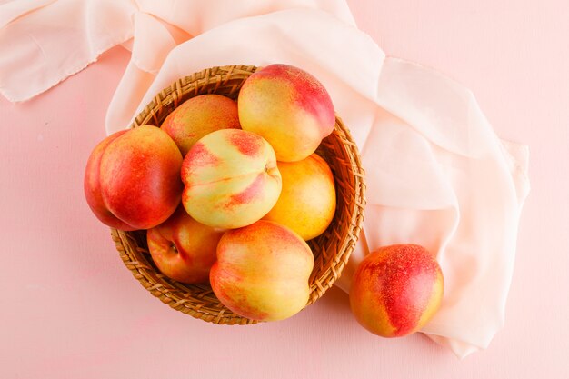 Free photo nectarines in a basket on pink and textile surface. top view.