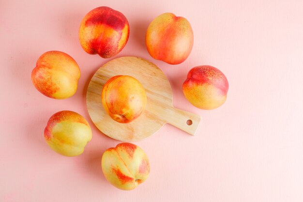 Nectarines on pink and cutting board table. flat lay.