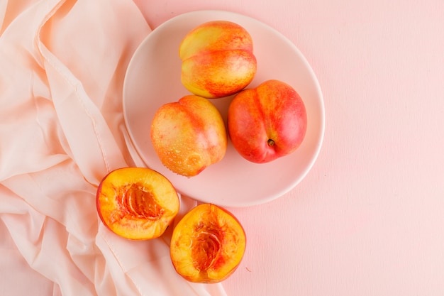 Nectarines in a plate on pink and textile surface. flat lay.