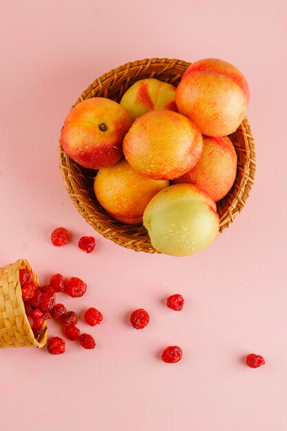 Nectarines with dried cherry in a basket on pink surface, top view.