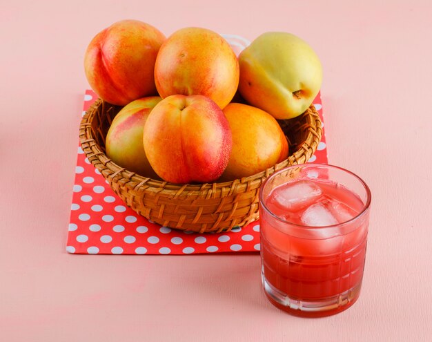 Nectarines with juice in a basket on pink and paper bag, high angle view.