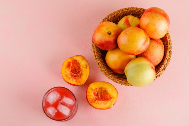 Nectarines with juice in a basket on pink surface, flat lay.