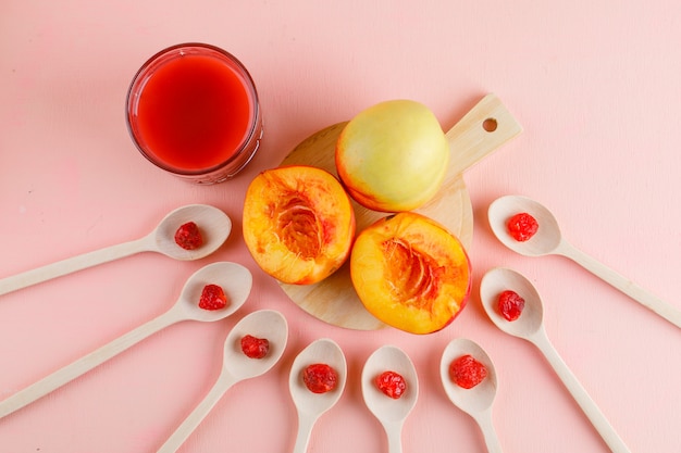 Nectarines with juice, dried cherry on pink and cutting board table, flat lay.