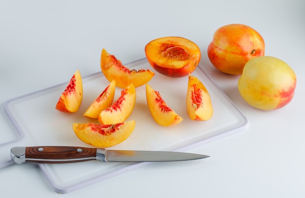 Foto gratuita nettarine con la vista dell'angolo alto del coltello sulla tavola del tagliere e di bianco