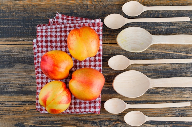 Le nettarine con cucchiai di legno piatti giacciono su un asciugamano di legno e cucina