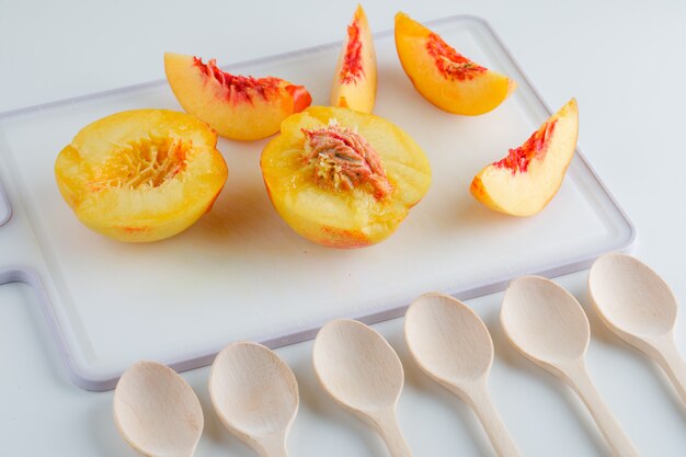 Nectarines with wooden spoons on white and cutting board table, high angle view.