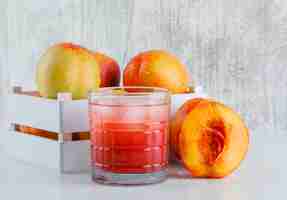 Free photo nectarines in a wooden box with juice side view on white and grungy wall