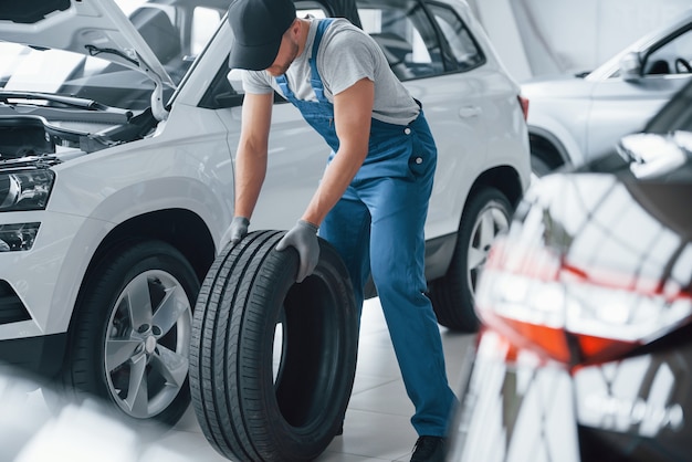 Foto gratuita hai bisogno di sbrigarti. meccanico che tiene un pneumatico al garage di riparazione. sostituzione di pneumatici invernali ed estivi