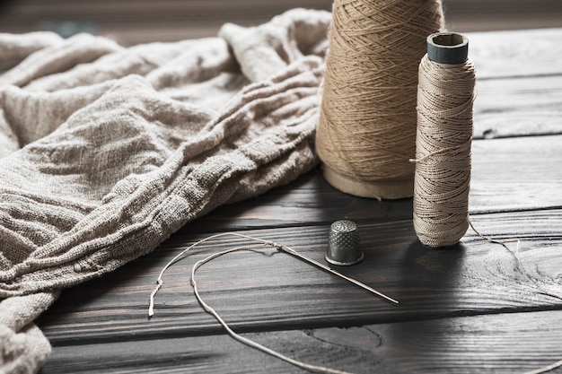 Needle; tread spool and thimble with jute fabric on wooden table