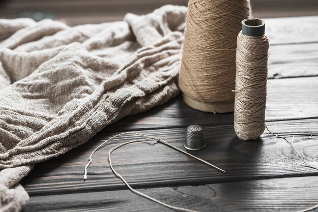 Needle; tread spool and thimble with jute fabric on wooden table