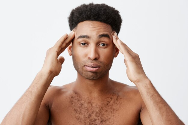 Negative emotions. Man having headache after partying all night. Close up of young dark-skinned male with afro hairstyle without clothes massaging head with hands.