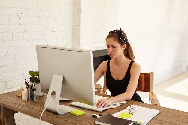 Negative human emotions. The upset female looks at the screen working at desk in front of computer in modern office. Tired designer or architect working at desk