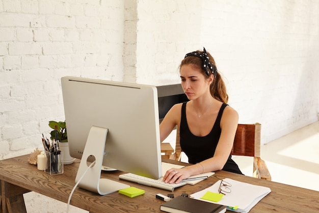 Negative human emotions. The upset female looks at the screen working at desk in front of computer in modern office. Tired designer or architect working at desk