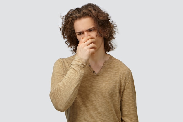 Free photo negative human expressions, feelings and reaction. picture of fashionable guy with wavy hair going to throw up, covering mouth with hand to suppress vomit because of disgusting smell or rotten food