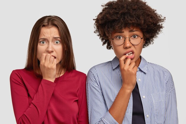 Nervous anxious two women bite finger nails with anxiety