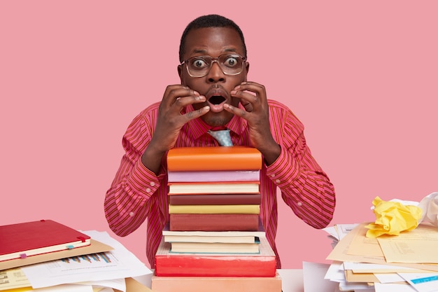 Nervous black college student looks in puzzlement, keeps hands near mouth, scared to read something, dressed in formal clothes