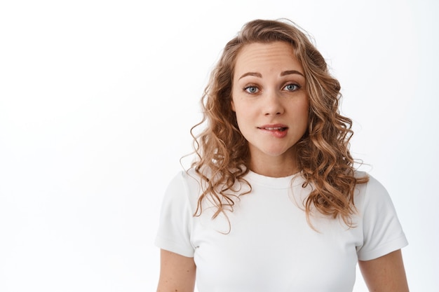 Free photo nervous blond girl biting lip and looking scared, making silly mistake, looking worried at front, standing against white wall