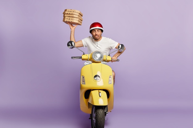 Nervous deliveryman driving scooter while holding pizza boxes