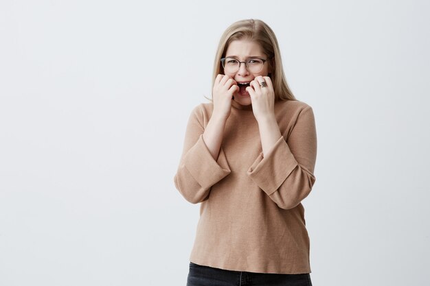 Nervous desperate upset female with blonde hair gestures with hands in anger, being irritated on boyfriend who is late for date. Sad woman hates something, shows negative emotions and feelings