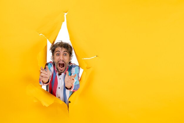Nervous and emotional young man poses in torn yellow paper hole background