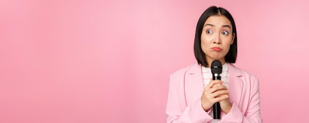 Nervous female entrepreneur giving speech with microphone holding mic and looking aside anxiously po