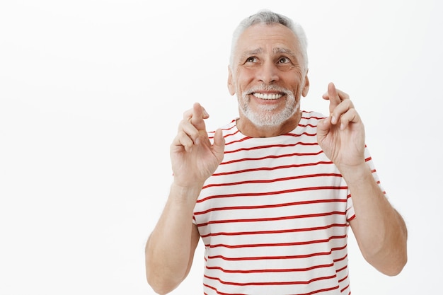 Nervous hopeful senior man cross fingers good luck and praying, making wish