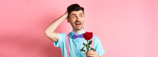 Nervous man waiting for his date on valentines day holding red rose and looking confused sideways sc