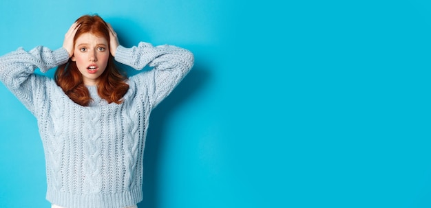 Ragazza rossa nervosa in piedi sopraffatta tenendosi per mano sulla testa in preda al panico e fissando il supporto della fotocamera