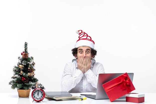 Nervous shocked young businessman with funny santa claus hat celebrating Christmas in the office on white background