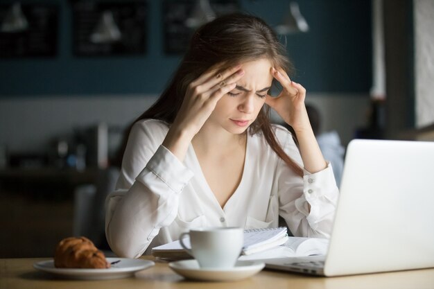 Nervous stressed female student feeling headache studying in cafe